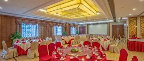 A banquet hall with round tables, red chairs, and a large screen.