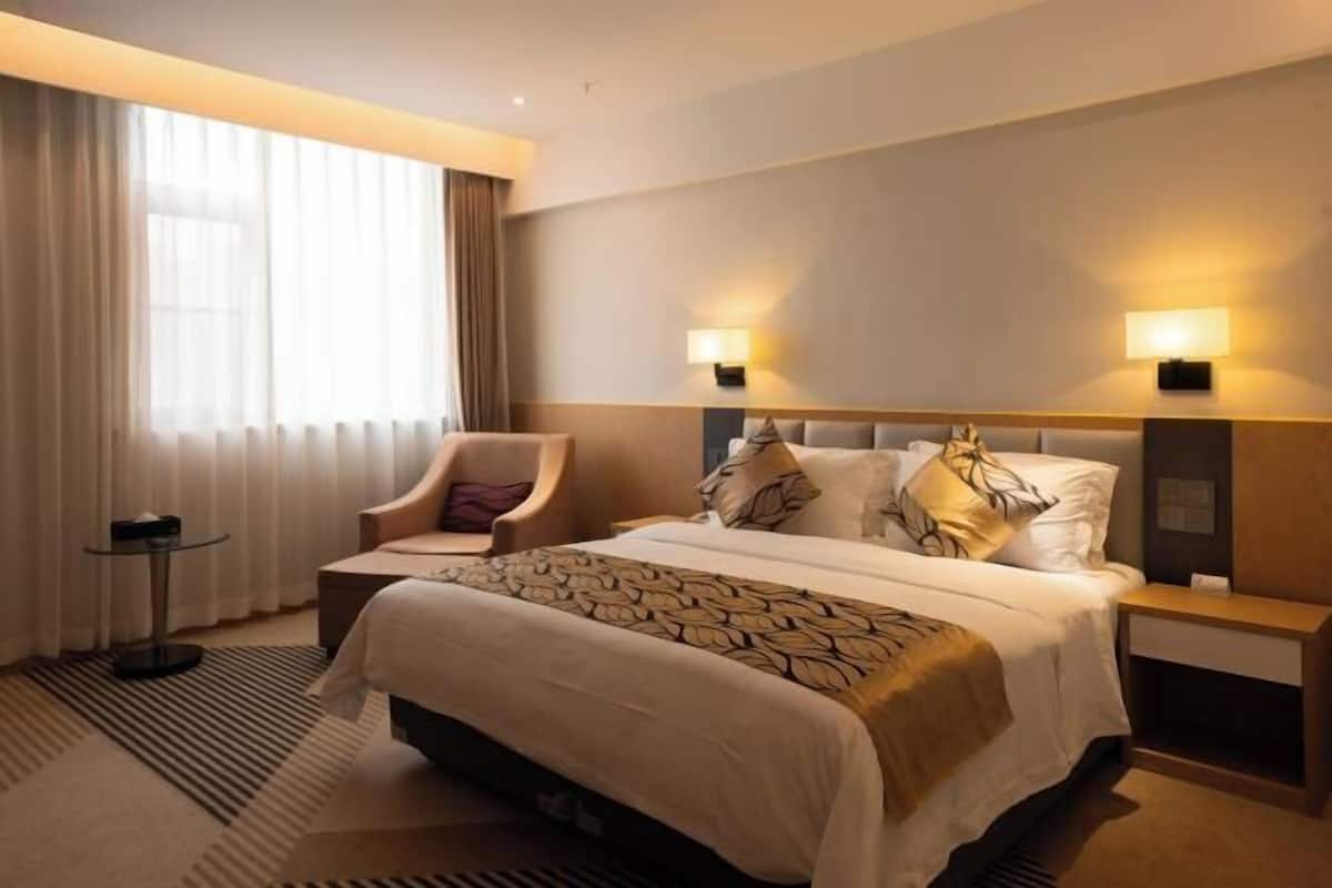 Habitación de hotel con una cama grande, dos lámparas de noche, una silla, una mesita y una ventana con cortinas.