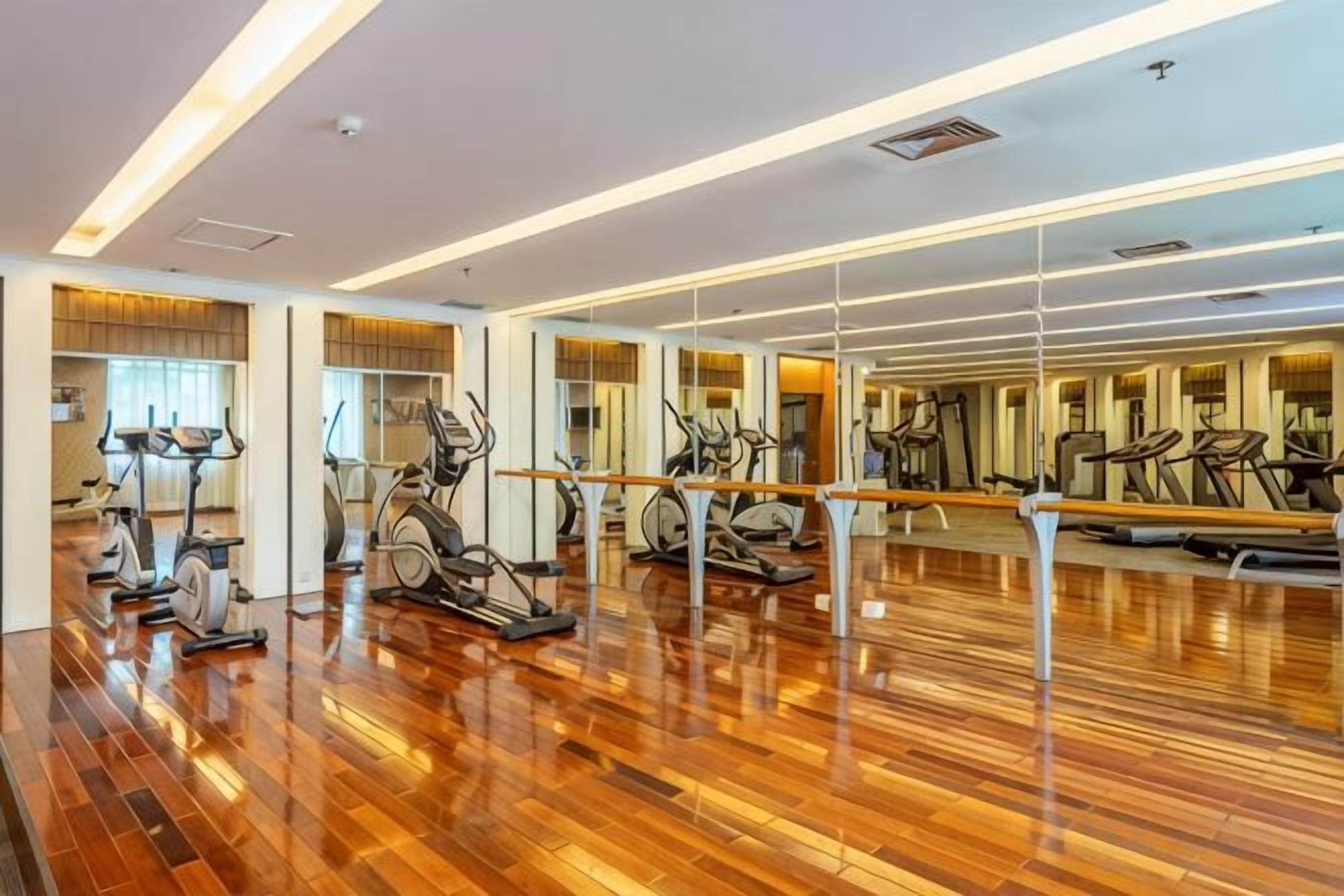 A gym with exercise equipment and mirrors on wooden floors.