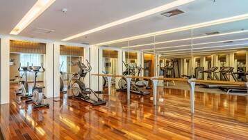 A gym with exercise equipment and mirrors on wooden floors.