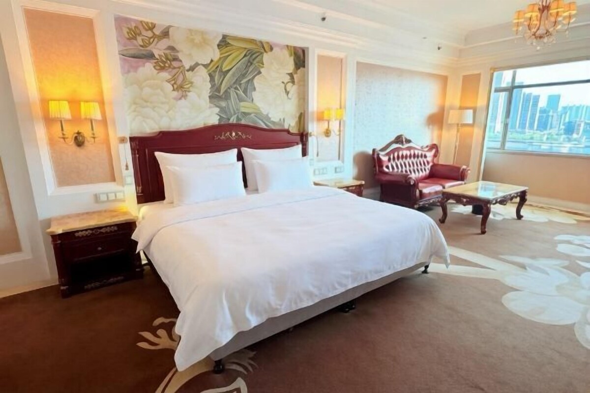 Een hotelkamer met een groot bed, een rode fauteuil, een klein tafeltje en uitzicht over de stad.