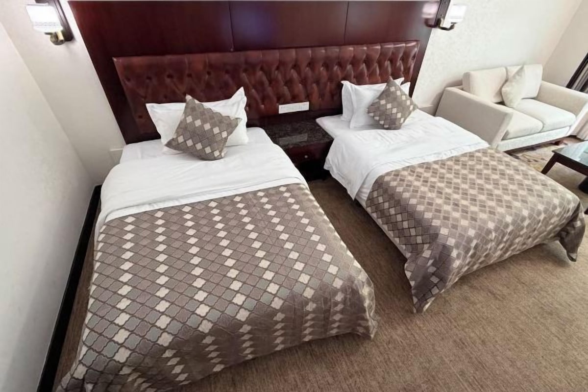 Une chambre d’hôtel avec deux lits, une tête de lit, un canapé et un sol recouvert de moquette.