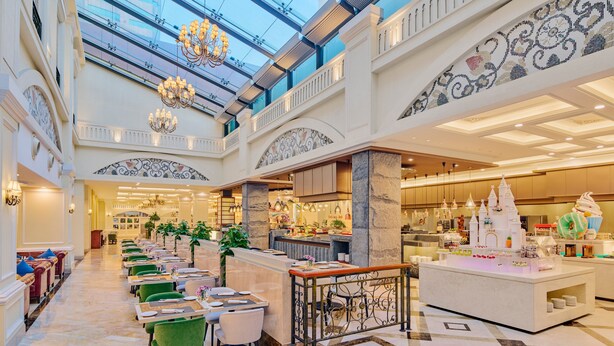 Eine Hotelhalle mit hoher Decke, Kristalllüstern, einer zentralen Bar und einer Treppe zu den oberen Etagen.