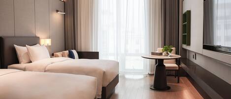 A hotel room with two beds, a small table with a plant, a TV, and a large window with curtains.
