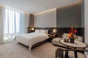 A hotel room with a large bed, a sofa, a round coffee table, and a nightstand with a lamp. - Hongshan Hotel (Wuhan)
