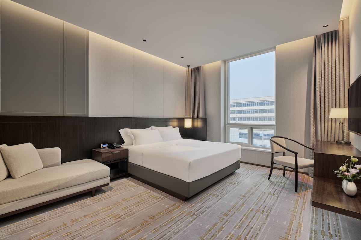 Una habitación de hotel moderna con una cama grande, un sofá, un escritorio y vistas de la ciudad.