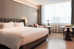 A hotel room with a large bed, a bedside table, a small round table, and a window with curtains. - Hongshan Hotel (Wuhan)