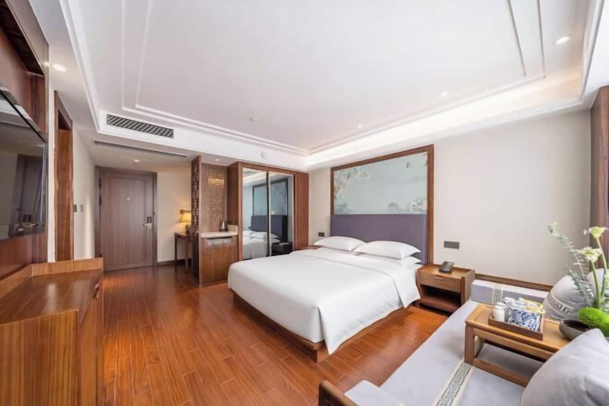 Une chambre d’hôtel avec un grand lit, un plancher en bois, un bureau avec une chaise, un miroir et une fenêtre.