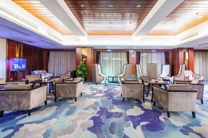 Un hall d’hôtel doté d’un sol recouvert de moquette, de plusieurs espaces aménagés avec des sièges et d’un téléviseur.