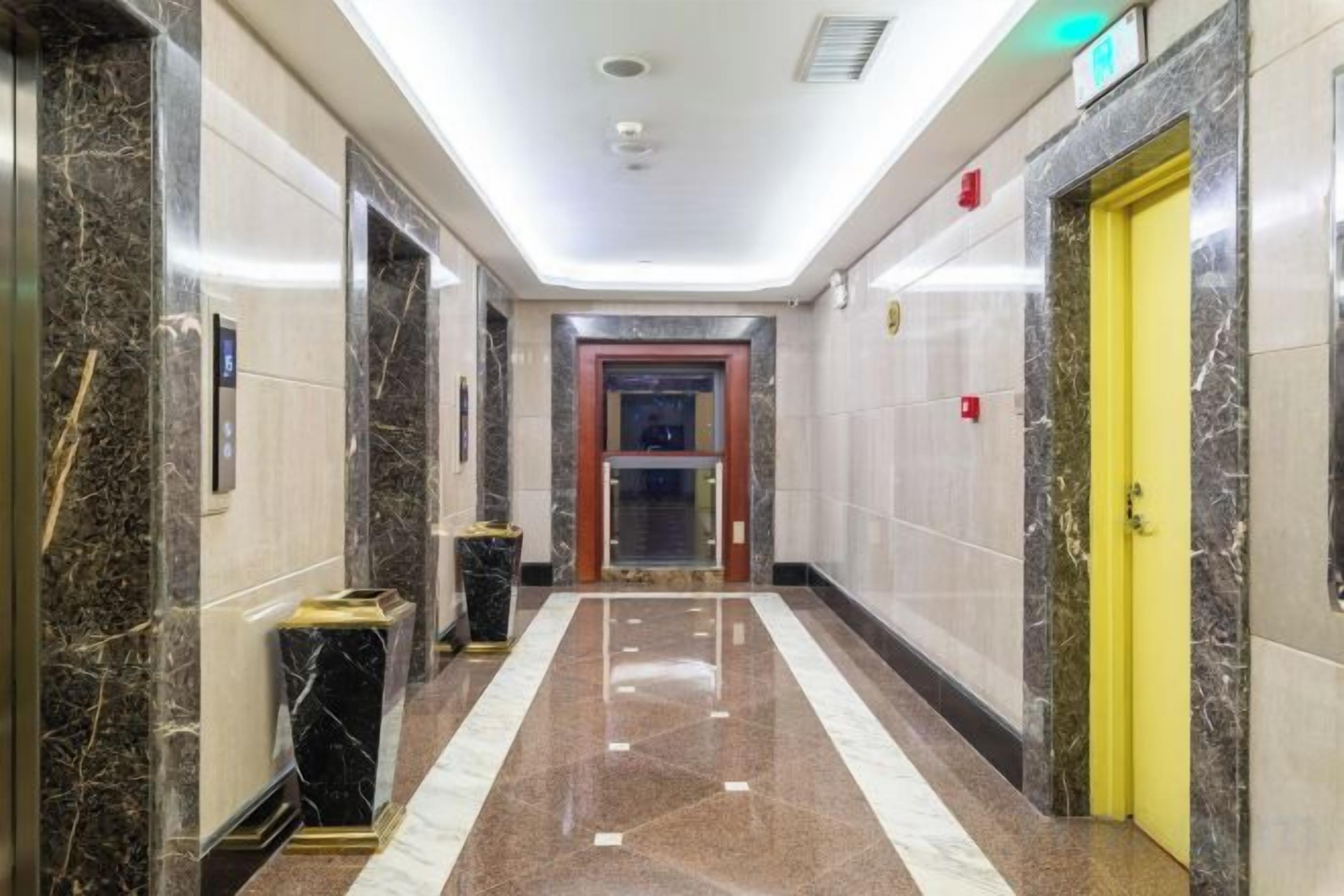 En hall med väggar klädda i marmor, en gul dörr och en röd dörr som leder till en hiss.