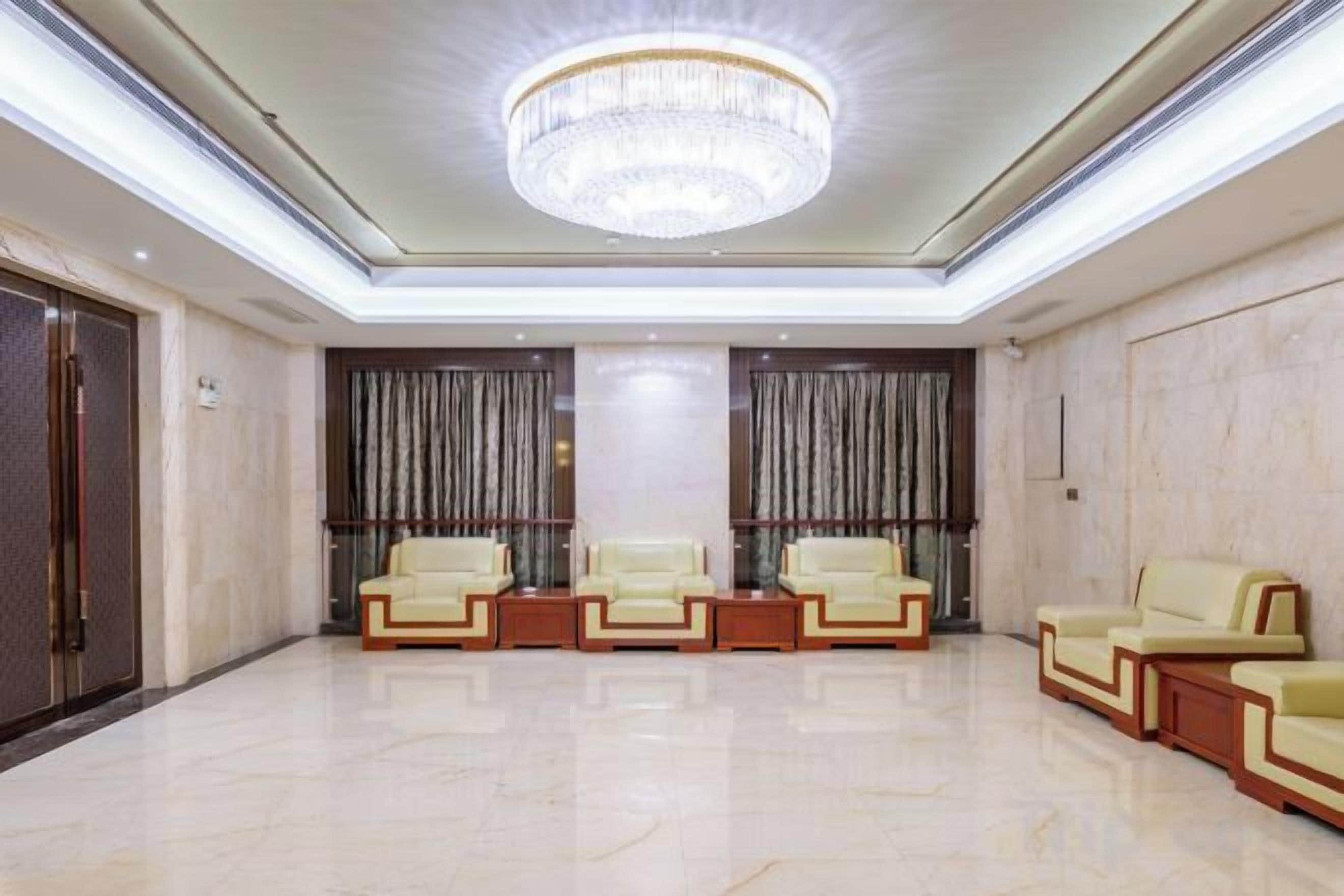 A spacious lobby with a chandelier, two rows of leather sofas, and a marble floor.