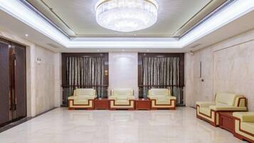 A spacious lobby with a chandelier, two rows of leather sofas, and a marble floor.