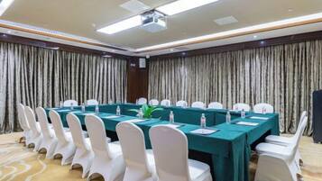 A conference room with a long table, white chairs, and a projector screen.
