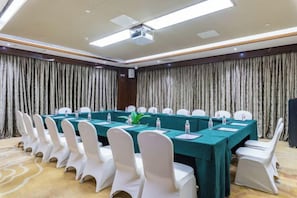 A conference room with a long table, white chairs, and a projector screen.