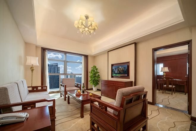 Une chambre d’hôtel équipée d’un canapé, d’un fauteuil, d’un bureau et d’une grande fenêtre donnant sur la ville.