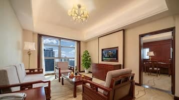 A hotel room with a sofa, armchair, desk, and a large window with a city view.