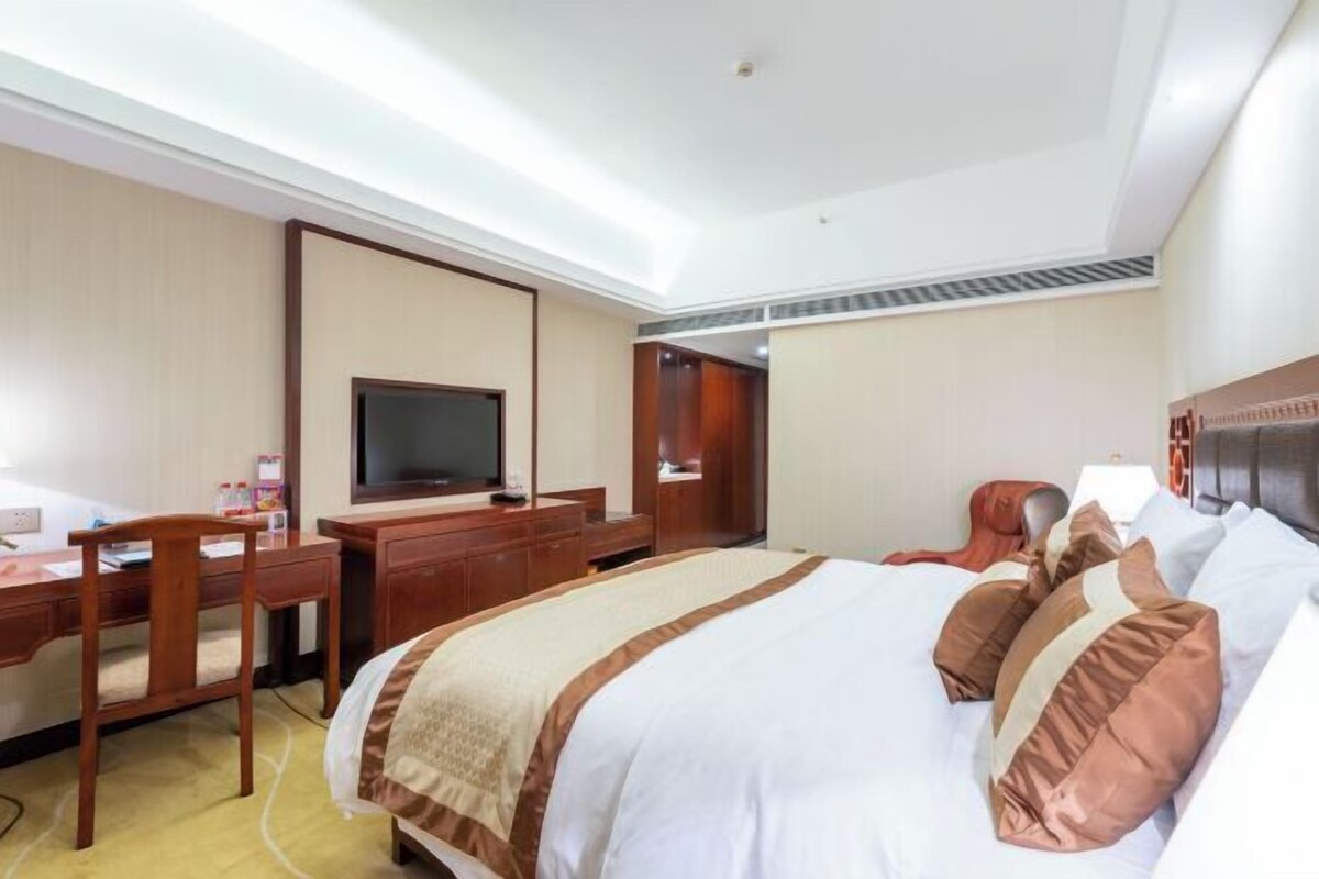 A hotel room with a bed, a desk, a chair, a television, and a wardrobe.