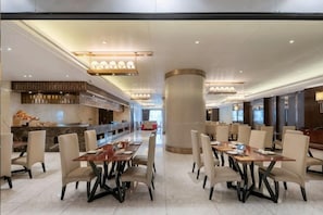 A spacious dining area with multiple tables and chairs, a central pillar, and a bar area in the background. - Tianlong Hotel (Changsha)