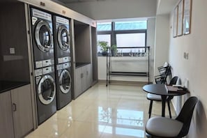 A laundry room with two washing machines, a table with chairs, and a view of the outdoors.
