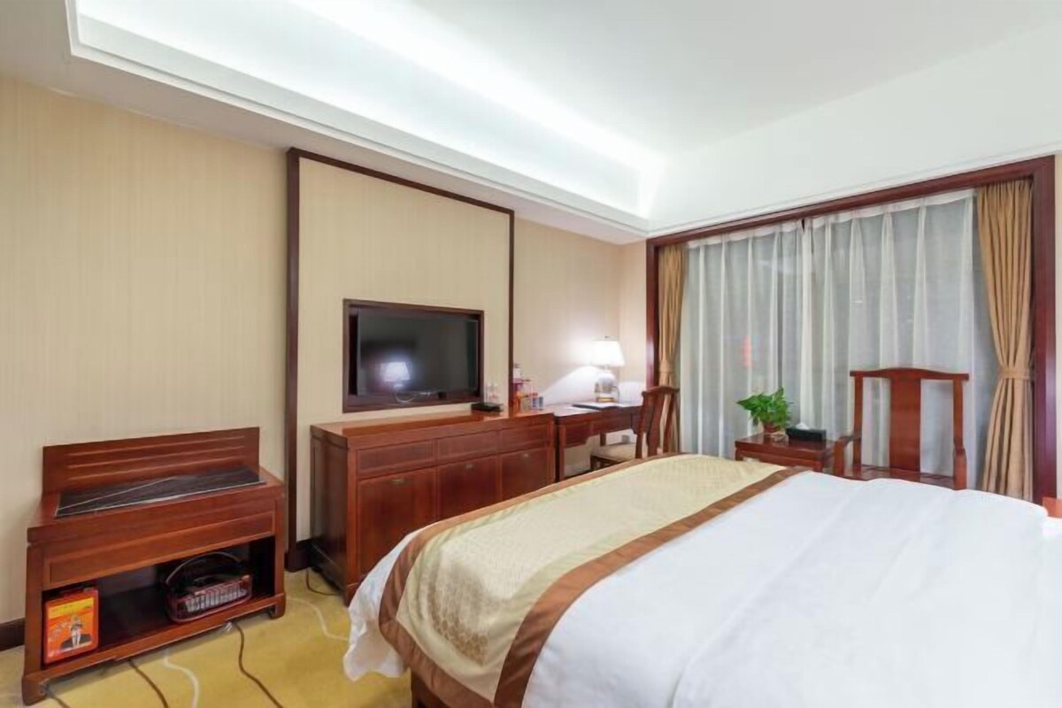 A hotel room with a bed, a desk, a television, and a small seating area.