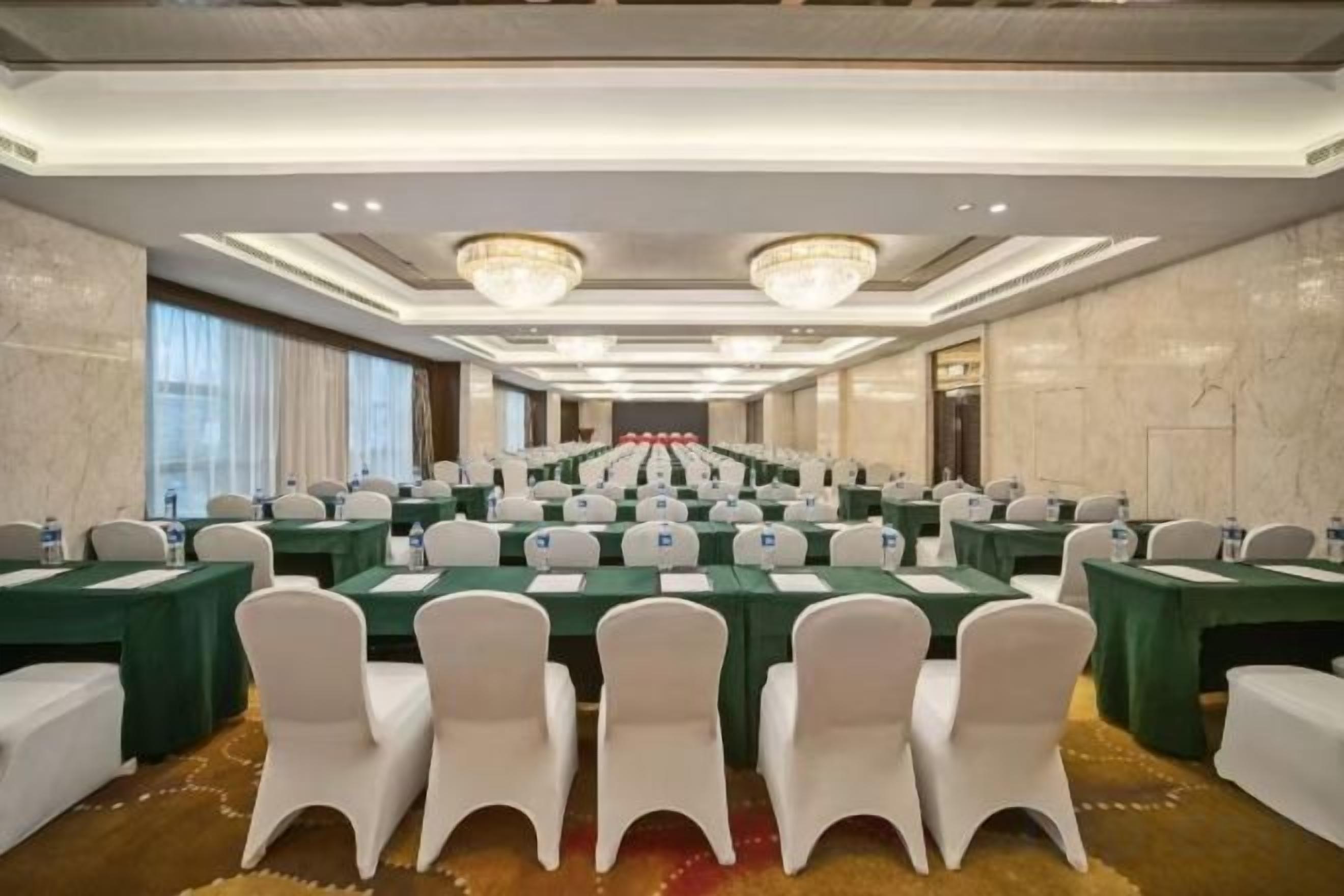 Un salón de conferencias con varias mesas y sillas, una araña y una pared de mármol.