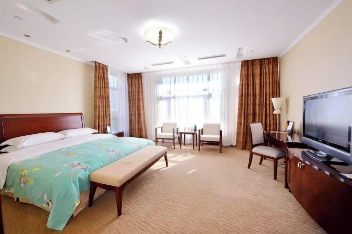 A hotel room with a bed, a desk, a television, and a window with curtains.