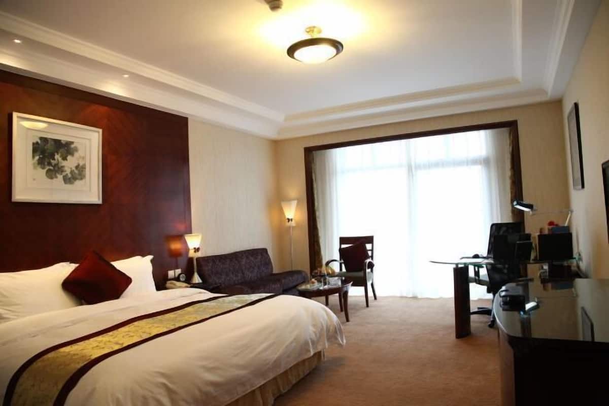 A hotel room with a large bed, a desk with a computer, a chair, and a sofa.