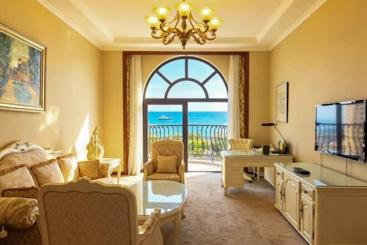 A room with a large window, a chandelier, a sofa, a table, and a TV.