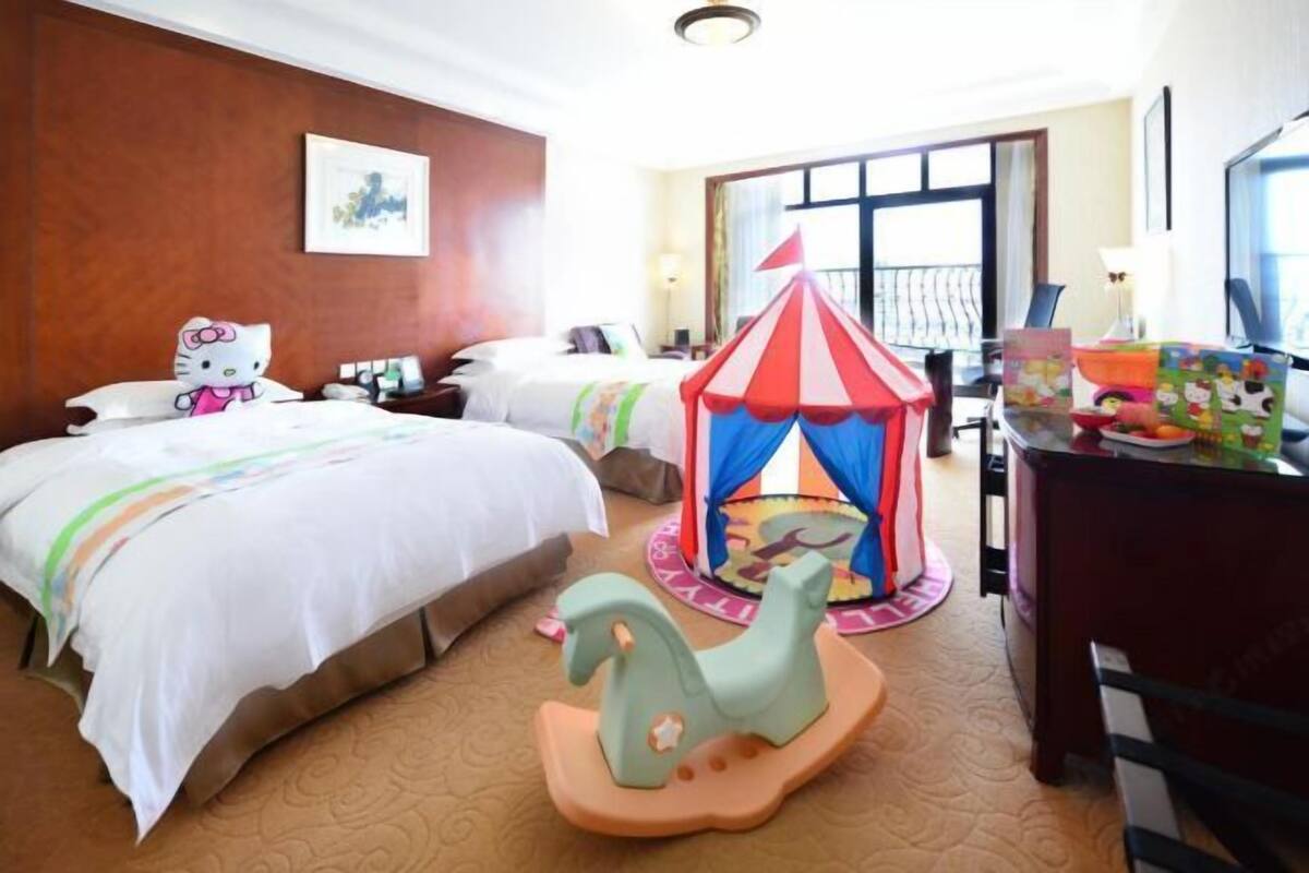 A hotel room with two beds, a Hello Kitty pillow, a carousel, and a desk with a lamp.