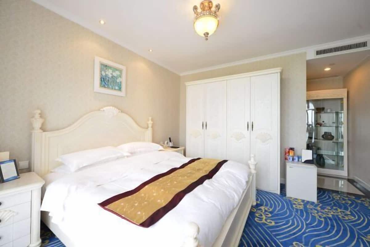 A hotel room with a large bed, white wardrobe, and a small desk with a lamp.