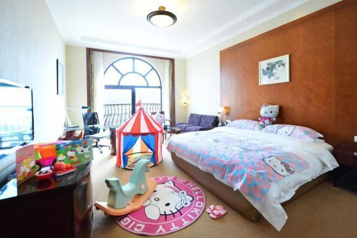 A hotel room with a bed, a desk, a Hello Kitty play tent, and a view of the outside.