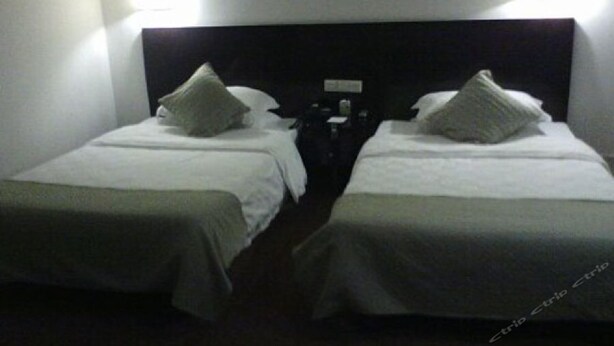 A hotel room with two single beds, each with a pillow and a nightstand. - Zhangjiagang Guomao Hotel (Suzhou)