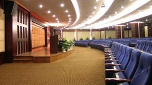 A conference room with rows of blue chairs, a podium, and a carpeted floor. - Zhangjiagang Guomao Hotel (Suzhou)