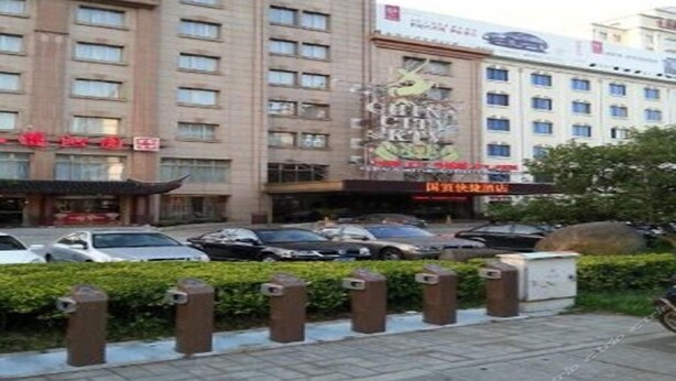 A multi-story hotel with a central courtyard, parking area, and a large advertisement on the building facade. - Zhangjiagang Guomao Hotel (Suzhou)