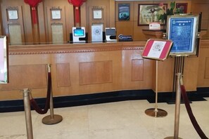 A reception desk with a wooden finish, a red velvet rope barrier, and a framed certificate on the wall. - Guilin Park Hotel (GUILIN)