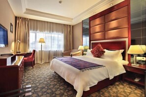 A hotel room with a large bed, a desk, a chair, a TV, and a window with curtains. - Guilin Park Hotel (GUILIN)