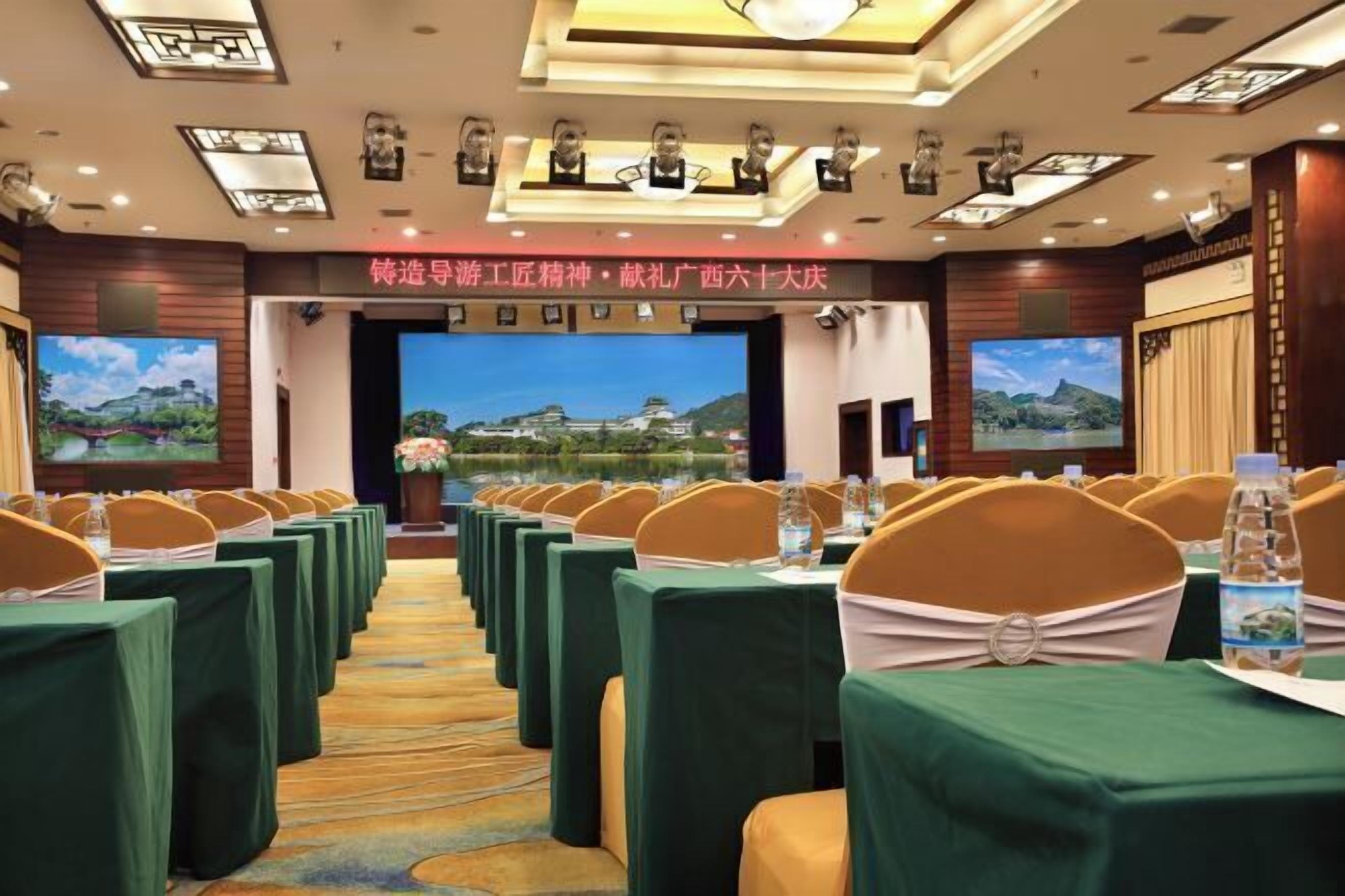 A conference room with rows of tables and chairs, a large screen at the front, and a banner with text.
