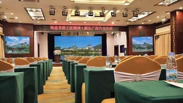A conference room with rows of tables and chairs, a large screen at the front, and a banner with text.