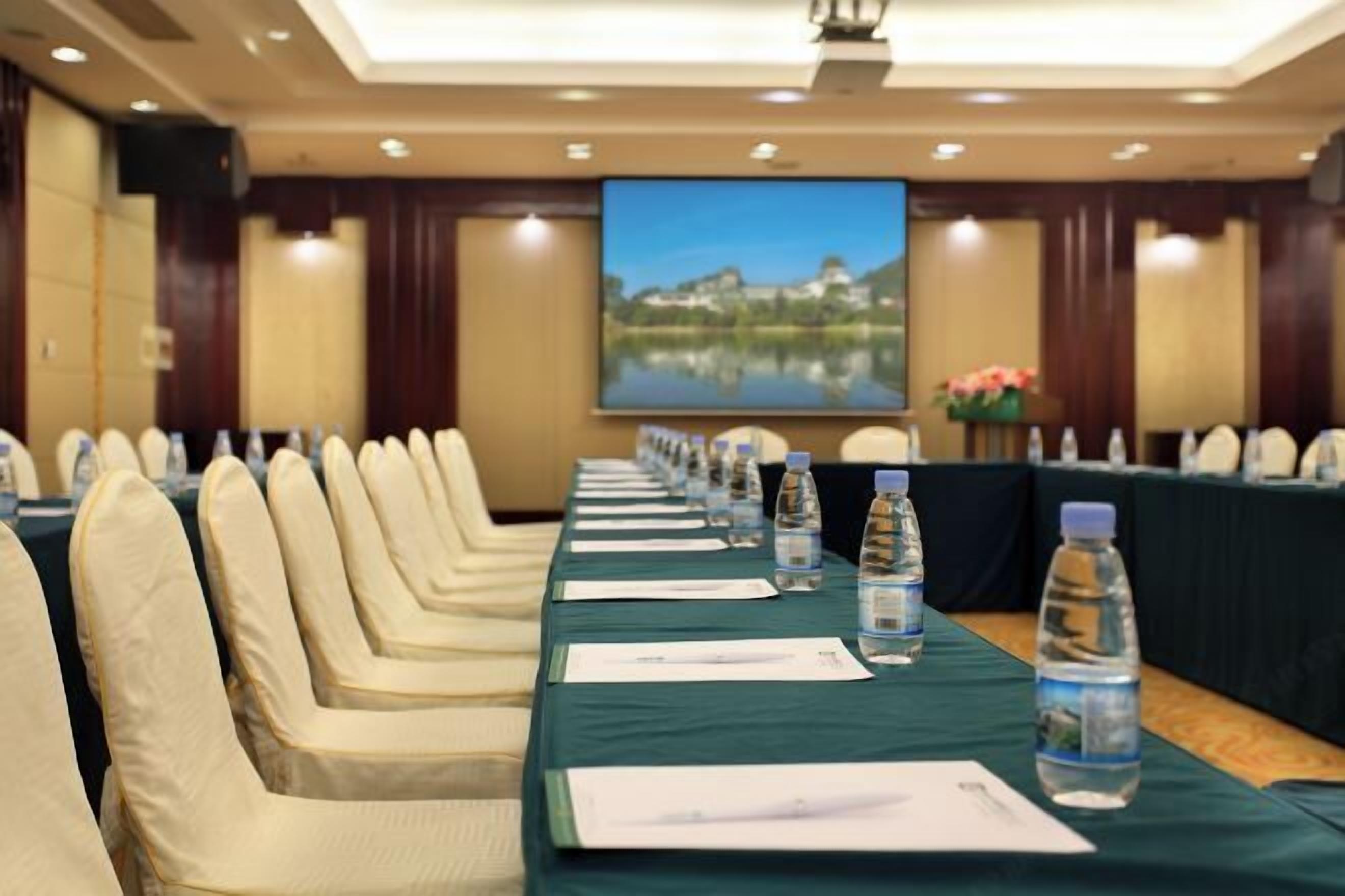A conference room with a long table, chairs, water bottles, and a large screen displaying a scenic view.
