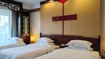 A hotel room with three beds, a decorative wall with a red accent, and a window with curtains.