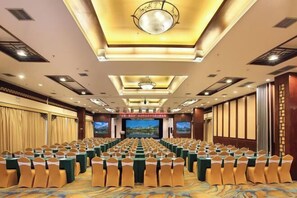 A conference room with rows of tables and chairs, a large screen, and a chandelier. - Guilin Park Hotel (GUILIN)