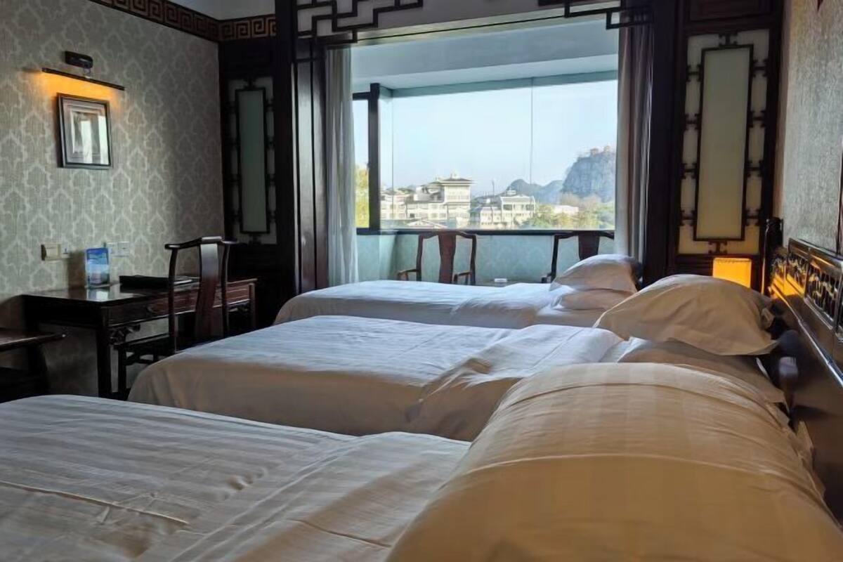 Habitació d'hotel amb dos llits, una taula de treball i vistes a edificis a través d'una finestra gran.