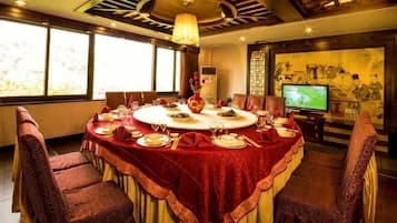A round dining table with a red tablecloth, surrounded by chairs, in a room with large windows and a television.