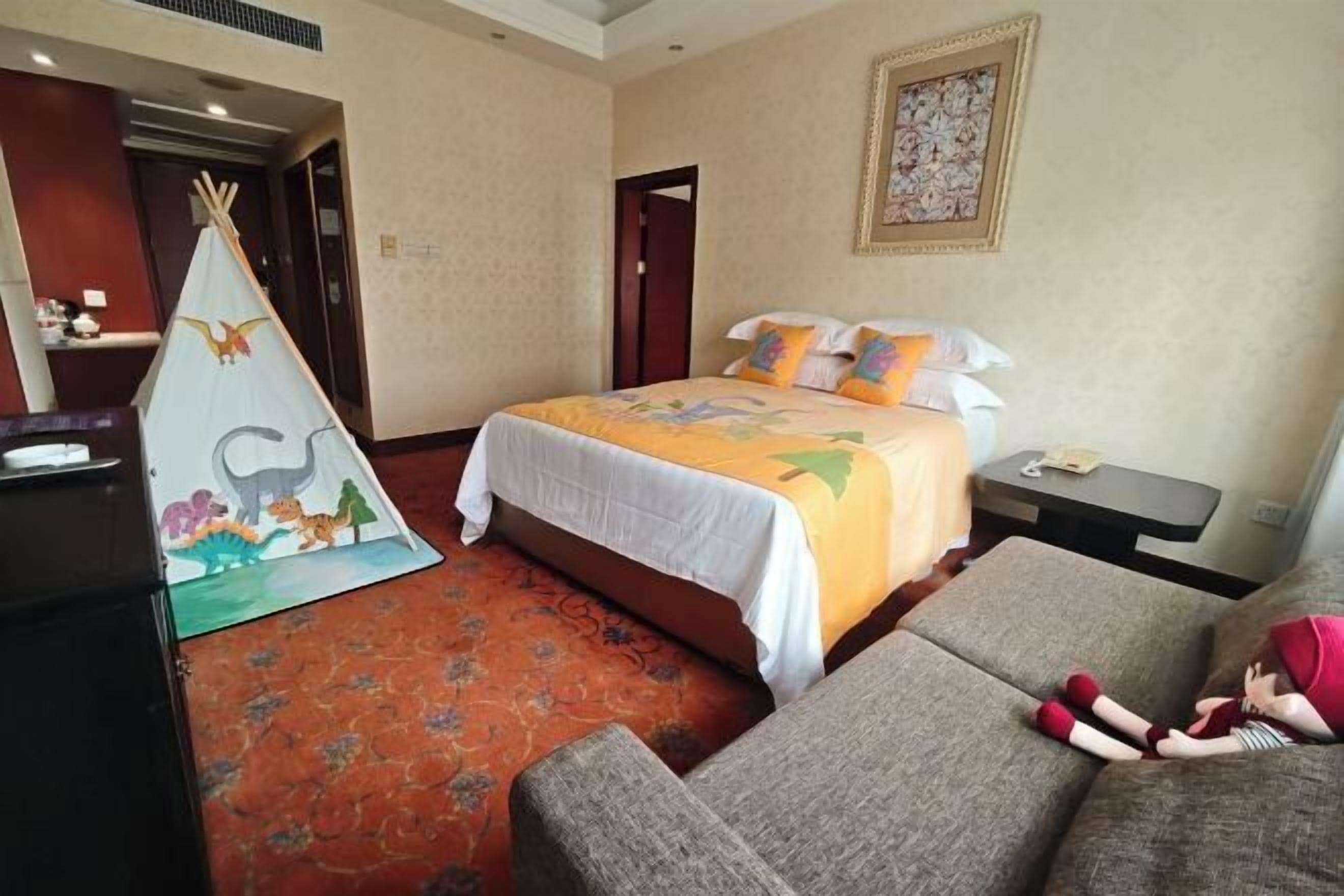 A hotel room with a bed, a sofa, a small table, a chair, a decorative teepee, and a wall painting.