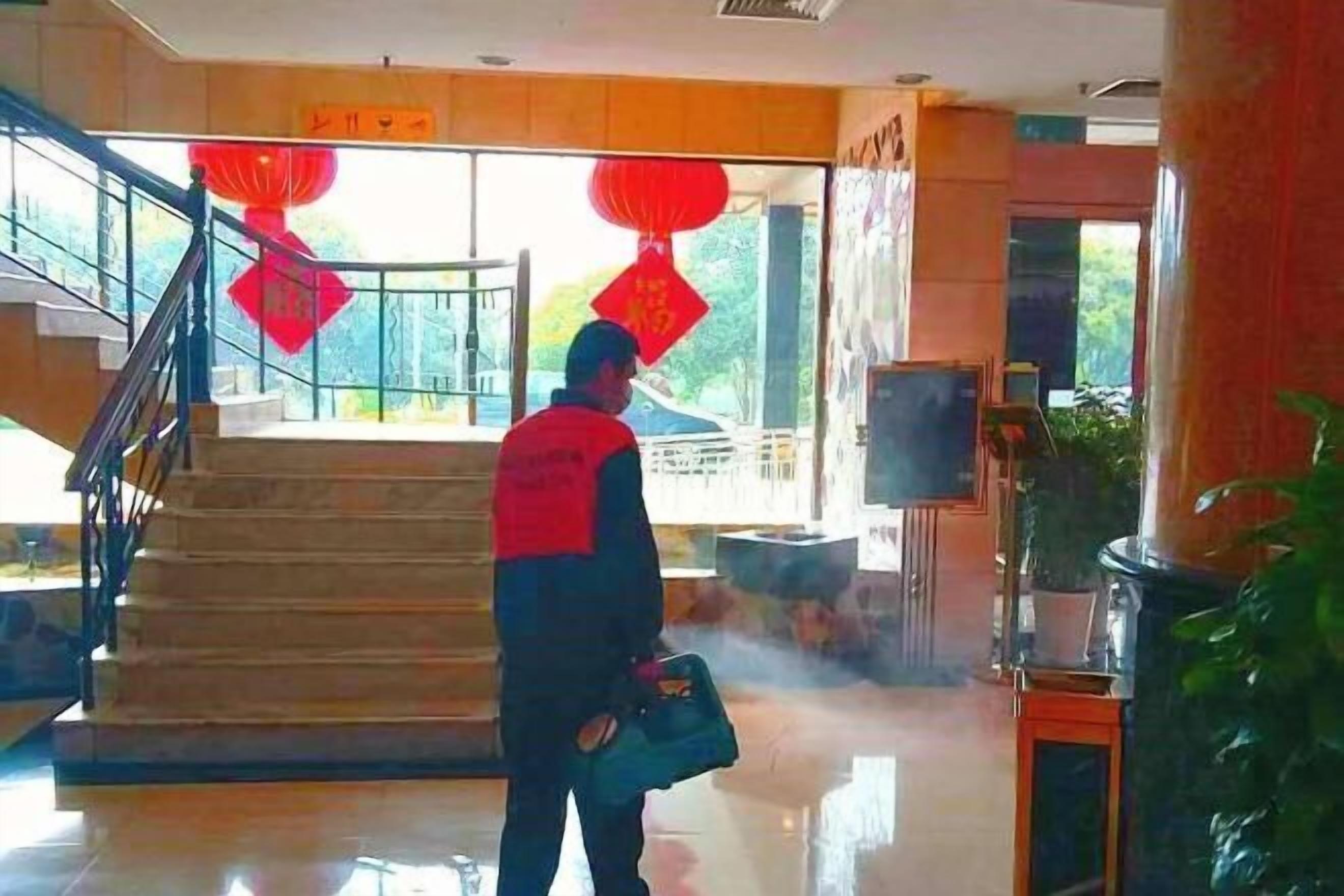 A person standing in a lobby with a staircase, red lanterns, and a large plant.