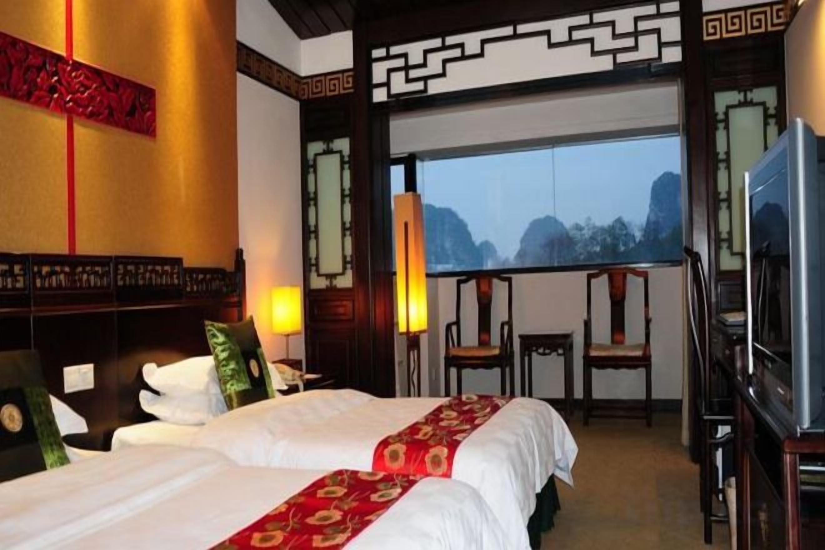 A hotel room with two beds, a TV, a desk, and a view of mountains.