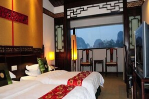 A hotel room with two beds, a TV, a desk, and a view of mountains. - Guilin Park Hotel (GUILIN)