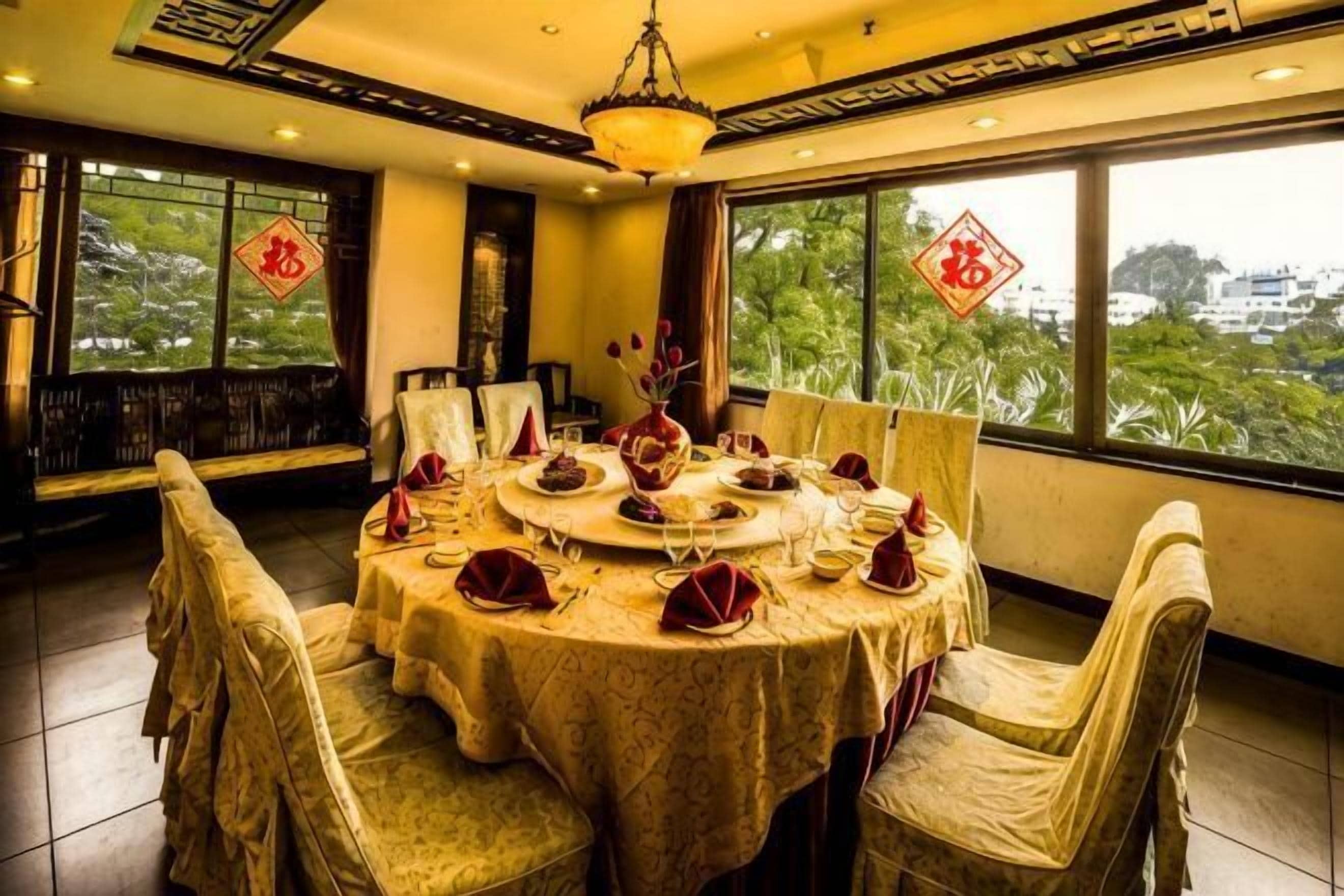 Un coin repas avec une table ronde dressée pour un repas, entourée de chaises, et offrant une vue sur la verdure à travers de grandes fenêtres.