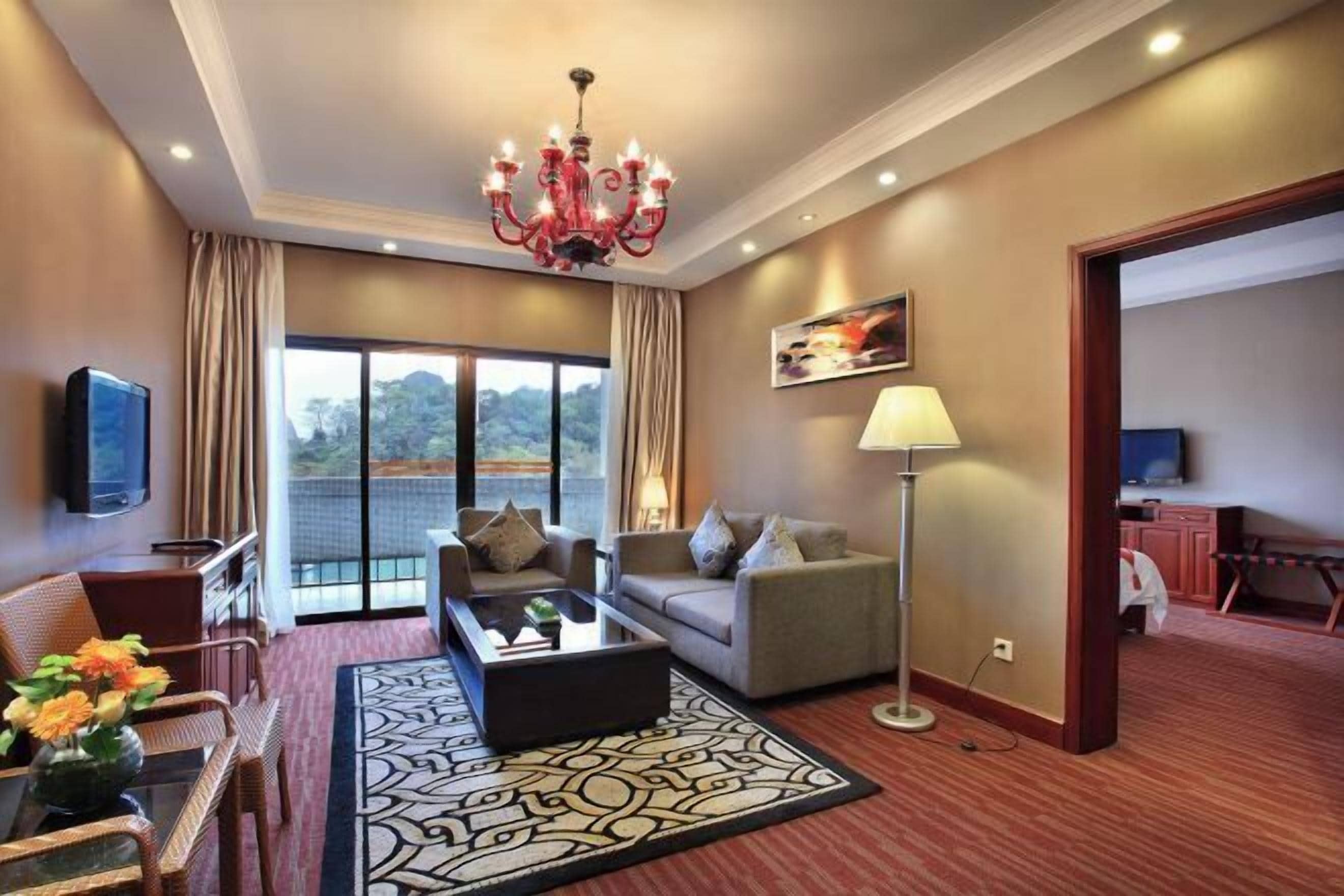 Une chambre d’hôtel moderne avec une grande fenêtre, un lustre, un canapé, une table basse et une lampe.