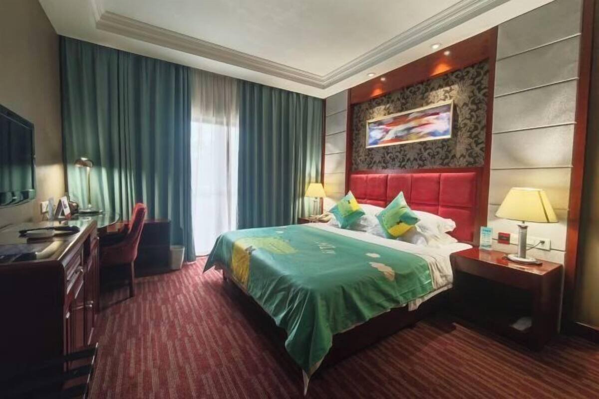 Habitació d'hotel amb un llit gran, un escriptori amb una cadira, un televisor i una finestra amb cortines.
